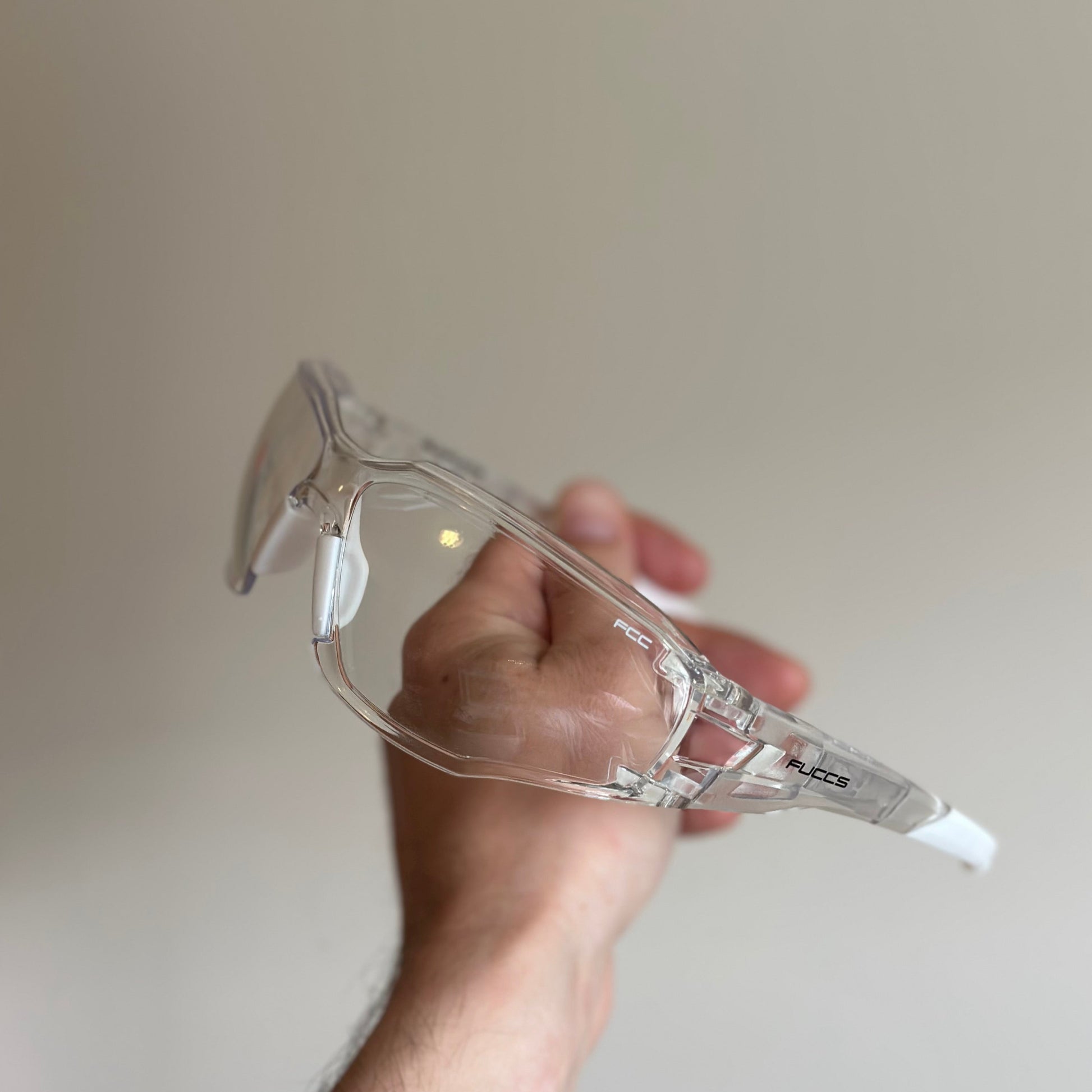 Hand holding a clear safety goggles against a plain background