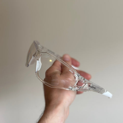 Hand holding a clear safety goggles against a plain background